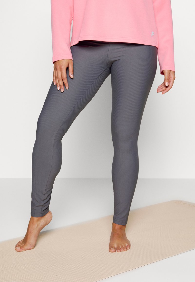 Leggings cinzentos com riscas e um design ajustado, combinados com uma blusa de mangas longas rosa, expostos sobre um tapete de yoga.