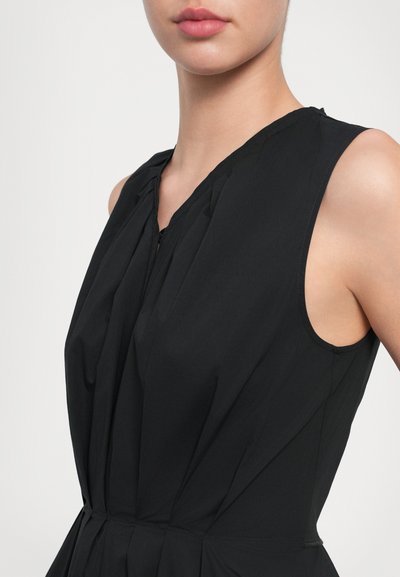 Vestido negro sin mangas con escote en V, detalles plisados y una textura suave. Presenta una cremallera discreta en el frente.