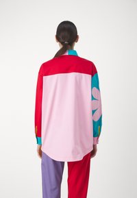 Long-sleeve shirt featuring a color-block design in red, pink, and turquoise, with a floral print on the left sleeve and button accents.