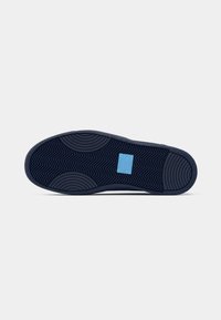 Blue sneaker sole featuring a wave-patterned tread and a rectangular blue logo patch; rubber material; rounded edges and textured surface detail.
