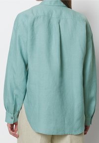 Camicia a maniche lunghe azzurro chiaro realizzata in tessuto morbido e testurizzato, con orlo curvo e polsini con bottone, caratterizzata da un dettaglio a yoke sul retro.