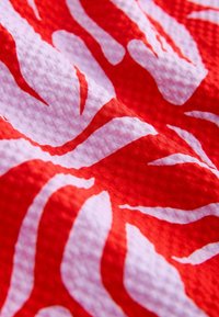 Nahaufnahme eines rot-weißen, strukturierten Stoffes mit abstrakten, unregelmäßigen Mustern und sichtbaren gewebten Oberflächendetails.