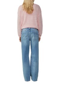 Lichtroze, gestructureerde gebreide trui met lange mouwen, gedragen over blauwe, high-waisted, wijde jeans met achterzakken en een vervaagde wassing.