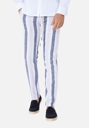 Pantaloni di lino con righe verticali blu e bianche, caratterizzati da una vita con cordoncino e tessuto leggero, abbinati a scarpe nere senza lacci.