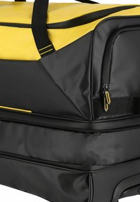 Borsa da viaggio nera e gialla con un design geometrico, realizzata in materiale resistente. Presenta cerniere gialle e manici neri per una presa sicura.