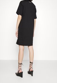 Svart kortärmad klänning med rak skärning, med sidofickor. Matchad med svarta kilklackar och crisscross-remmar runt anklarna.