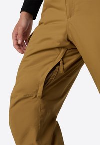 Brune vandtætte bukser med en lynlåslomme og glat tekstur, med en tætsiddende pasform og forstærkede sømme.