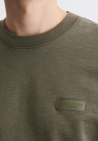 Bawełniana bluza w kolorze oliwkowej zieleni z okrągłym dekoltem, ściągaczami na rękawach oraz teksturowaną prostokątną metką z wytłoczonym napisem "Marc O'Polo".