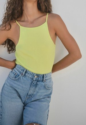 Żółty prążkowany top na ramiączkach z cienkimi paskami, zestawiony z wysokimi niebieskimi szortami dżinsowymi z surowym wykończeniem i wyblakłym odcieniem.