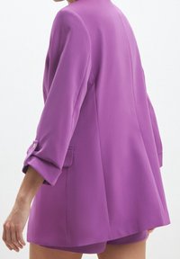 Lila blazer med avslappnad passform, uppvikta ärmar och två sidofickor. Slät yta och lättviktig tyg för lager-på-lager.