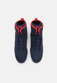High-top athletic shoes in navy mesh with red accents. Features include a textured surface, reinforced eyelets, and a pull tab on the collar.