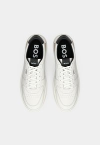 Pair of white leather BOSS sneakers with laces, black heel accent, and logo printed on tongue, sides, and insoles, viewed from above.