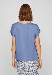 Blå kortermet topp i et mykt, lett stoff med en avslappet passform. Rund hals og oppbrettede ermer, kombinert med et skjørt med blomstermønster.