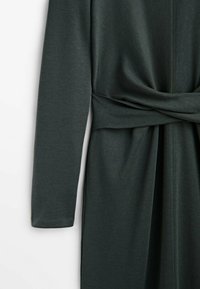 Robe longue à manches longues vert foncé avec une ceinture en tissu nouée à la taille, mettant en valeur les détails des manches et de la taille.