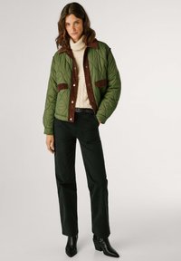 Gequilted groene bomberjack met een bruine corduroy kraag en zakken, gecombineerd met een crèmekleurige coltrui en zwarte wijde broek.