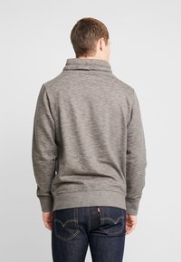Grå sweatshirts med høj krave, ribbet kant og blød tekstur. Båret med mørk denim jeans med baglomme-syning detaljer.