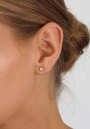 Rose gold stud earrings in a floral design, featuring four small clear crystals arranged in a square, set against a textured ear.