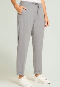 Graue, maßgeschneiderte Hose mit Tunnelzug in der Taille, seitlichen Taschen und gekrempelten Säumen, getragen mit weißen Turnschuhen. Glatte Textur und lässiges Design.