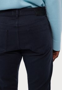 Pantaloni din denim bleu marin cu un finisaj texturat, având două buzunare la spate și o etichetă din piele neagră pe talie.