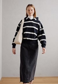 Felpa con cappuccio a righe bianche e nere abbinata a una gonna lunga in denim nera e a una borsa a tracolla color crema. Design semplice e casual, vestibilità rilassata.