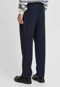 Navy blue trousers with a relaxed fit, elastic waistband, and back pockets; smooth fabric with a subtle texture, paired with black shoes.
