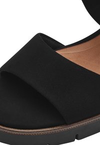 Sandal in suede nero con punta scoperta e design a fascia larga. La suola ha una finitura marrone chiaro, che offre un contrasto con la parte superiore nera.