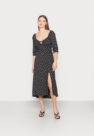 Vestido preto com estampa floral, com decote arredondado, mangas curtas bufantes e uma fenda alta na coxa. Apresenta um detalhe de buraco à frente.