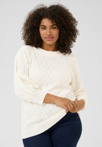 Pull en tricot blanc avec un motif en vagues, manches longues et coupe décontractée. Tissu texturé avec un col et un ourlet côtelés.