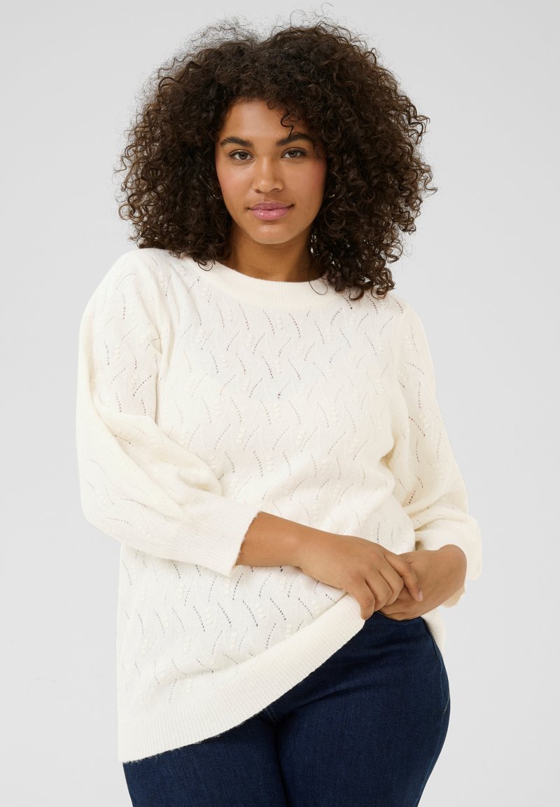 Pull en tricot blanc avec un motif en vagues, manches longues et coupe décontractée. Tissu texturé avec un col et un ourlet côtelés.