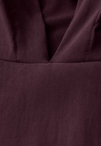 Tissu bourgogne avec une texture lisse et un décolleté en V profond, mettant en valeur des détails de couture subtils aux coutures.