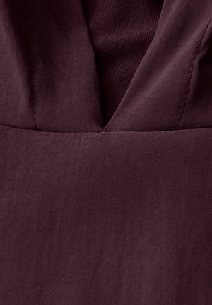 Burgundy fabric featuring a smooth texture with a deep V neckline, showcasing subtle stitching details at the seams.