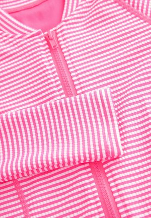 Růžový pruhovaný zipový oděv s měkkou texturou; má střídající se tenké bílé a růžové pruhy, viditelný zip a zaoblený límec.