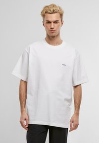 Hvit oversized T-skjorte laget av bomull, med rund hals og korte ermer. Liten blå brodert tekst på brystet.