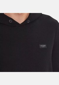 Sudadera negra de tejido suave, con un diseño de cuello en V y capucha con cordón. Pequeño logo cuadrado negro en el pecho.