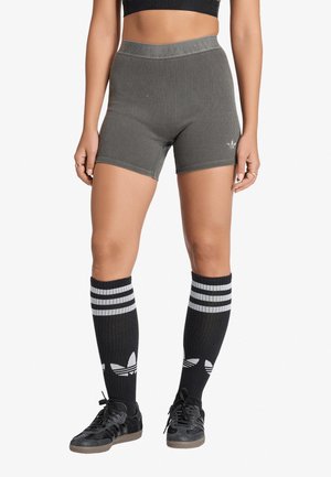 Donna che indossa pantaloncini grigi a coste a vita alta, calzini neri Adidas al ginocchio con strisce bianche e scarpe da ginnastica Adidas nere.
