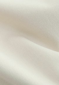 Nahaufnahme eines glatten, hellbeigen Stoffes mit feiner diagonaler Webstruktur und weichen Falten, die sanfte Schatten erzeugen.