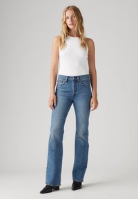 Vit ärmlös topp i kombination med ljusblå utsvängda jeans, med standard midjeband och minimalistisk design. Svarta skor fulländar outfiten.