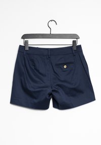Marinblå shorts i slät tyg, med en bakficka med en guldklick och två framfickor, hängande på en svart galge.