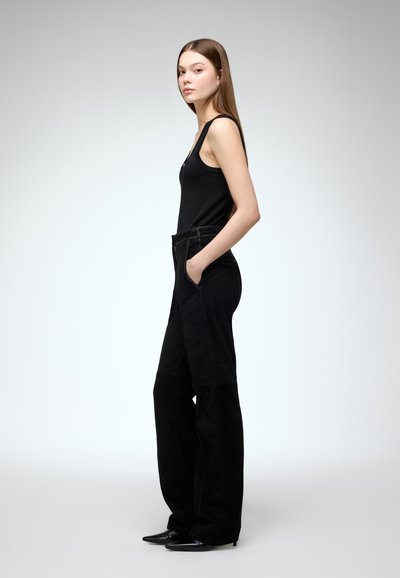 Zwarte tanktop gecombineerd met hoge, zwarte wide-leg broek met voorzakken en een zachte textuur; model staat in profiel.