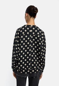 Czarny sweatshirt z dużymi beżowymi kropkami. Posiada okrągły dekolt i luźny fason, z prążkowanymi mankietami i dołem.