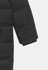 Rukáv černé péřové bundy s prošívaným designem, elastickým manžetovým zakončením a hladkou texturou. Obsahuje prošívané části pro zvýšenou izolaci.