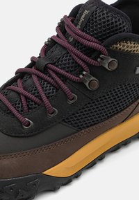 Chaussure de randonnée noire et marron avec des accents en maille, des lacets roses, un capuchon de protection pour les orteils et une semelle en caoutchouc texturée pour une meilleure adhérence.