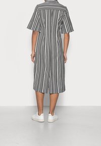 Robe chemise rayée en noir et blanc avec des manches courtes, longueur genou, design avec col, présentant une fente arrière et portée avec des baskets blanches.