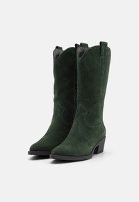 Botas de vaquero verde de ante con punta afilada, costuras decorativas, tacón bajo cuadrado y lengüetas en la parte superior del tubo.