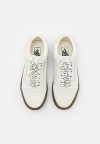 White sneakers with a textured upper, black and white laces, and brown rubber soles, featuring a subtle design accent along the side.