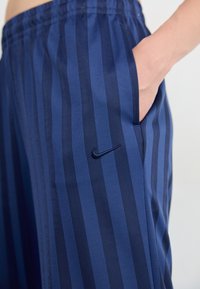 Pantalon à rayures bleu marine en tissu texturé. Équipé d'une taille élastique, de poches latérales et d'un petit logo Nike bleu marine sur la cuisse.