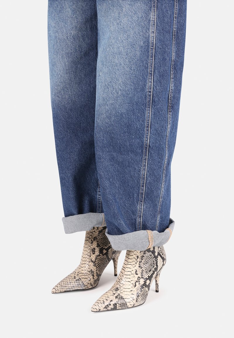Boty na vysokém podpatku s špičatou špičkou z texturované hadí kůže spárované s ohrnutými modrými džíny, které mají světle modré manžety.