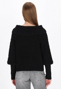 Czarny sweter dzianinowy z teksturowanym, bąbelkowym wzorem i szerokim dekoltem typu off-the-shoulder. Długie, prążkowane rękawy i krótki krój.