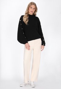 Maglione nero a coste con maniche a palloncino e dettagli in oro. Abbinato a pantaloni larghi crema e sneakers bianche.