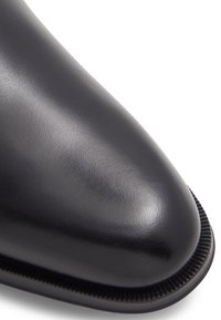 Scarpa in pelle nera con finitura liscia, punta affusolata e cuciture decorative lungo il bordo della suola. Texture sottile visibile.